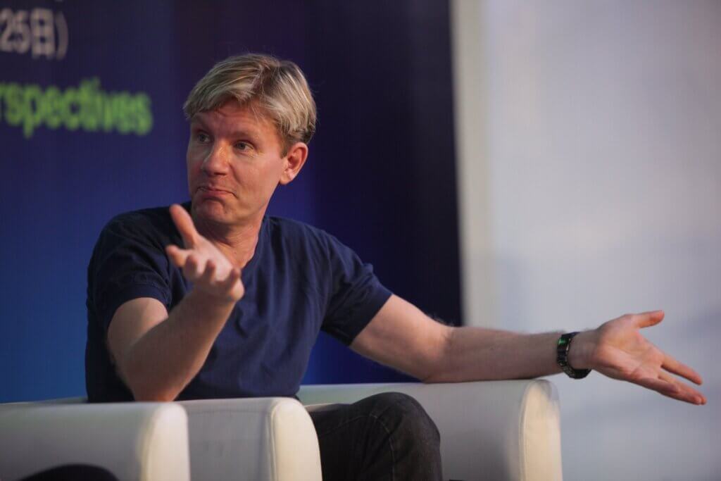 Bjørn Lomborg sitting in an armchair on what appears to be a stage at a symposium.